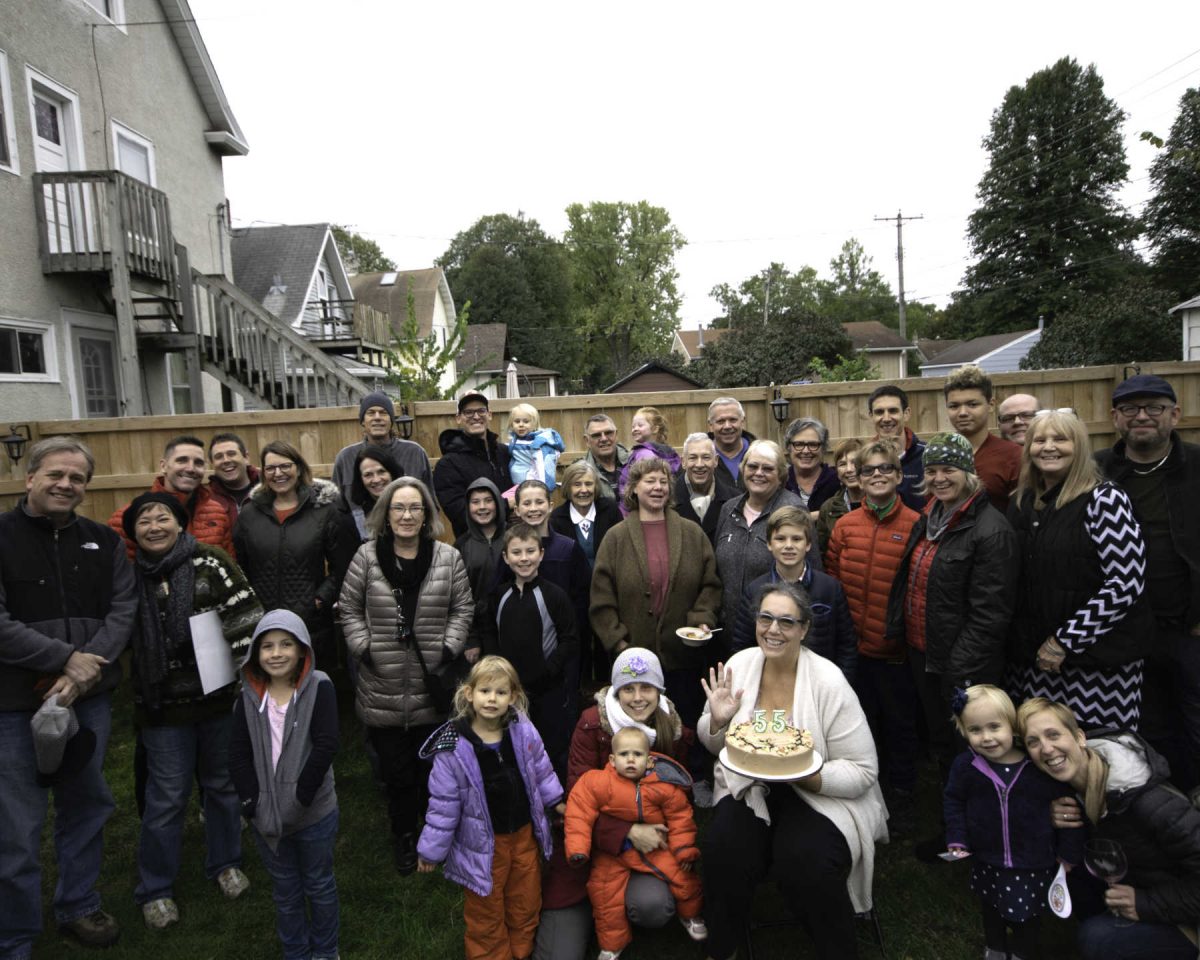 large group of people in backyard with 65 on a birthday cake