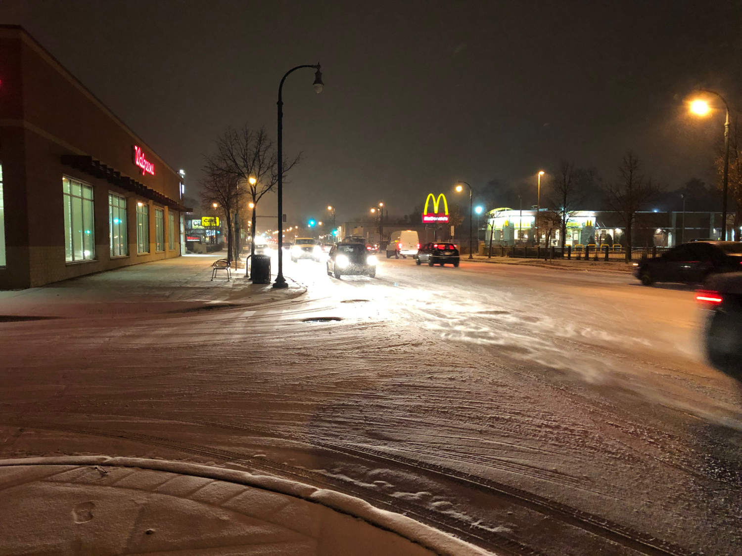 snowy scene of cars on street with Walgreens and McDonalds signs at night