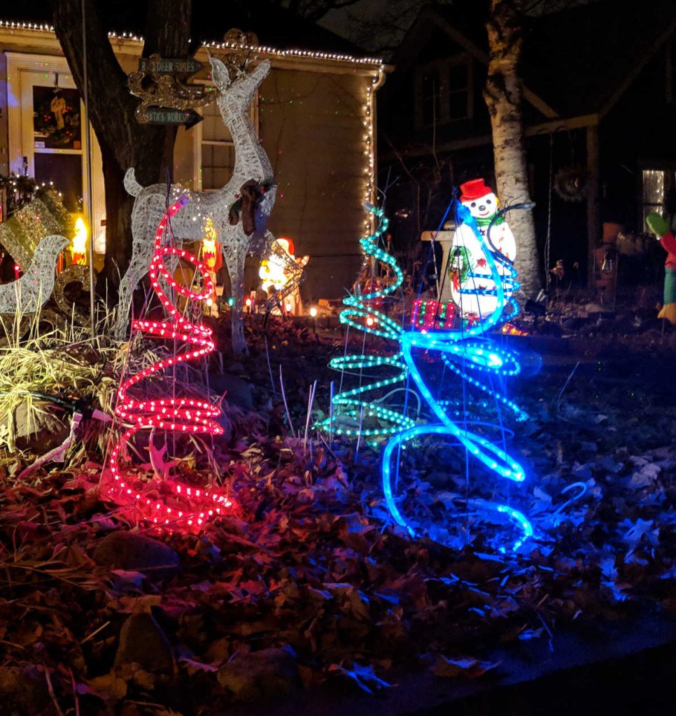 Lighted trees and snowman in holiday display in yard at night