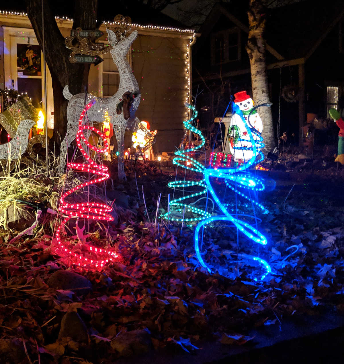 Lighted trees and snowman in holiday display in yard at night
