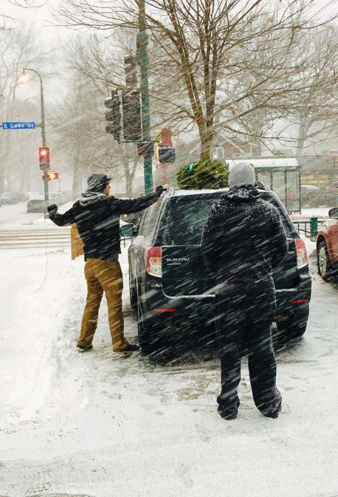 man tying christmas tree to top of car in a snow storm