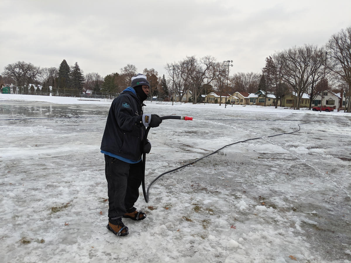 man with a water hose on ice in a park