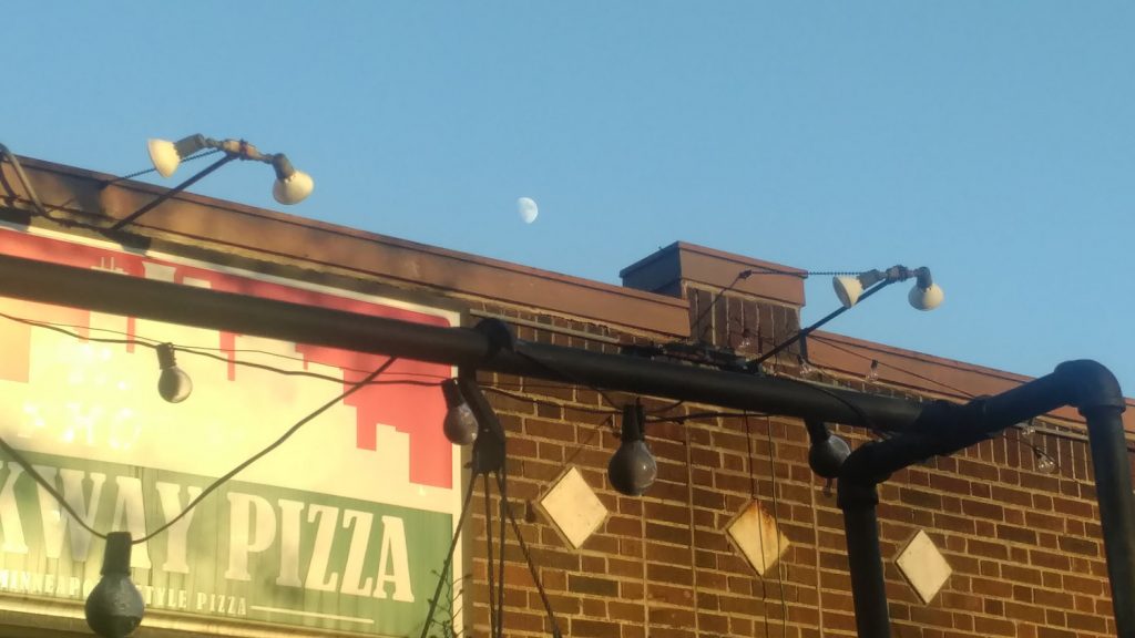 rising moon in blue sky over brick wall with pizza sign