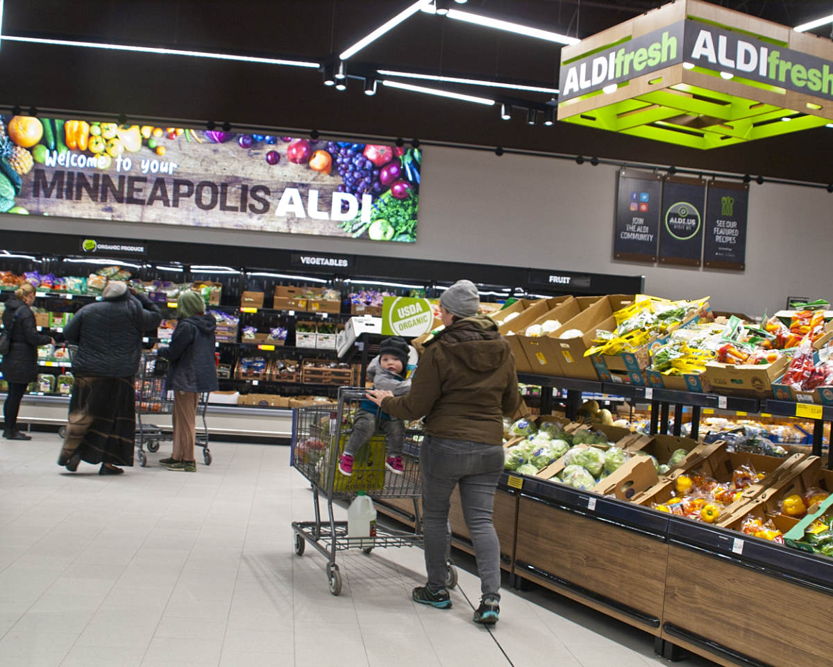 grocery shopper in aisle next to vegetables with Aldifresh sign overhead