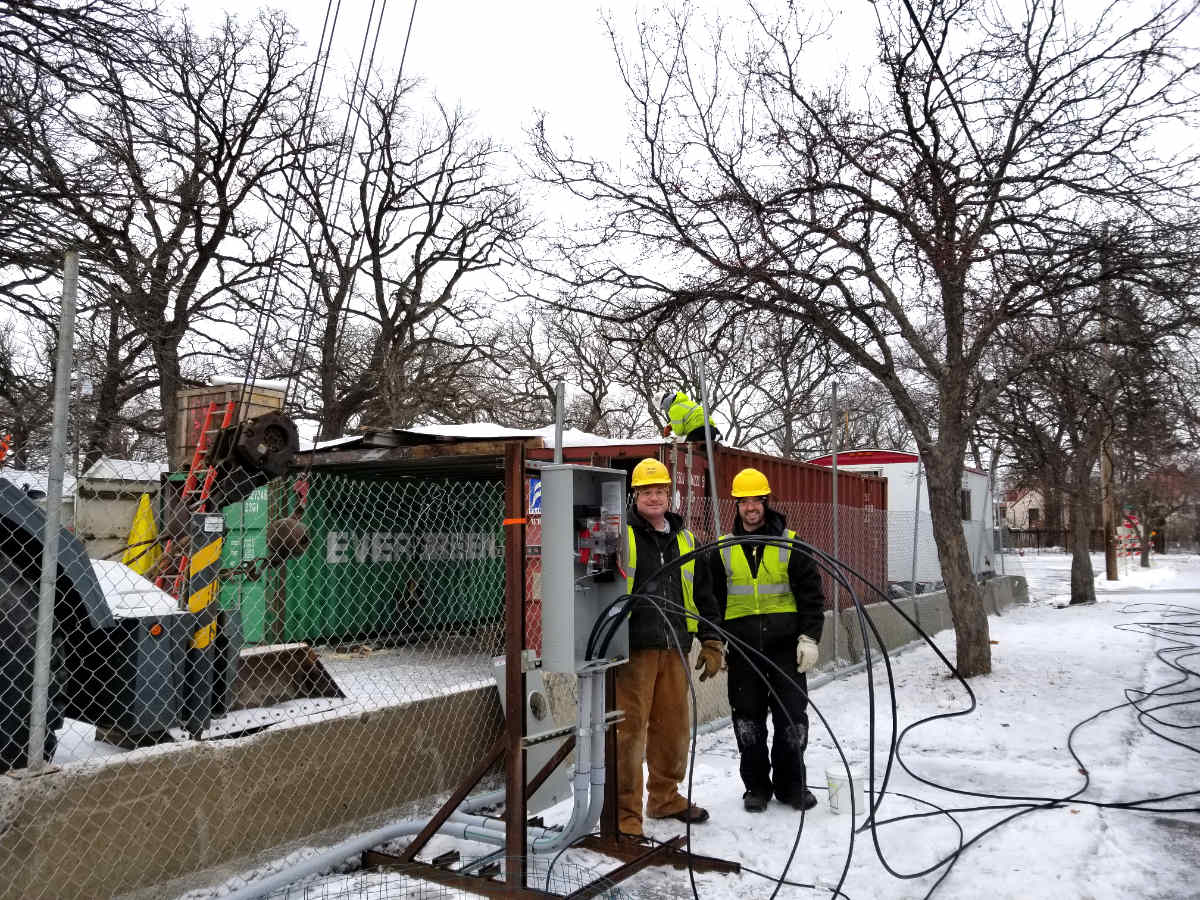two construction workers with electrical box and big long black cords