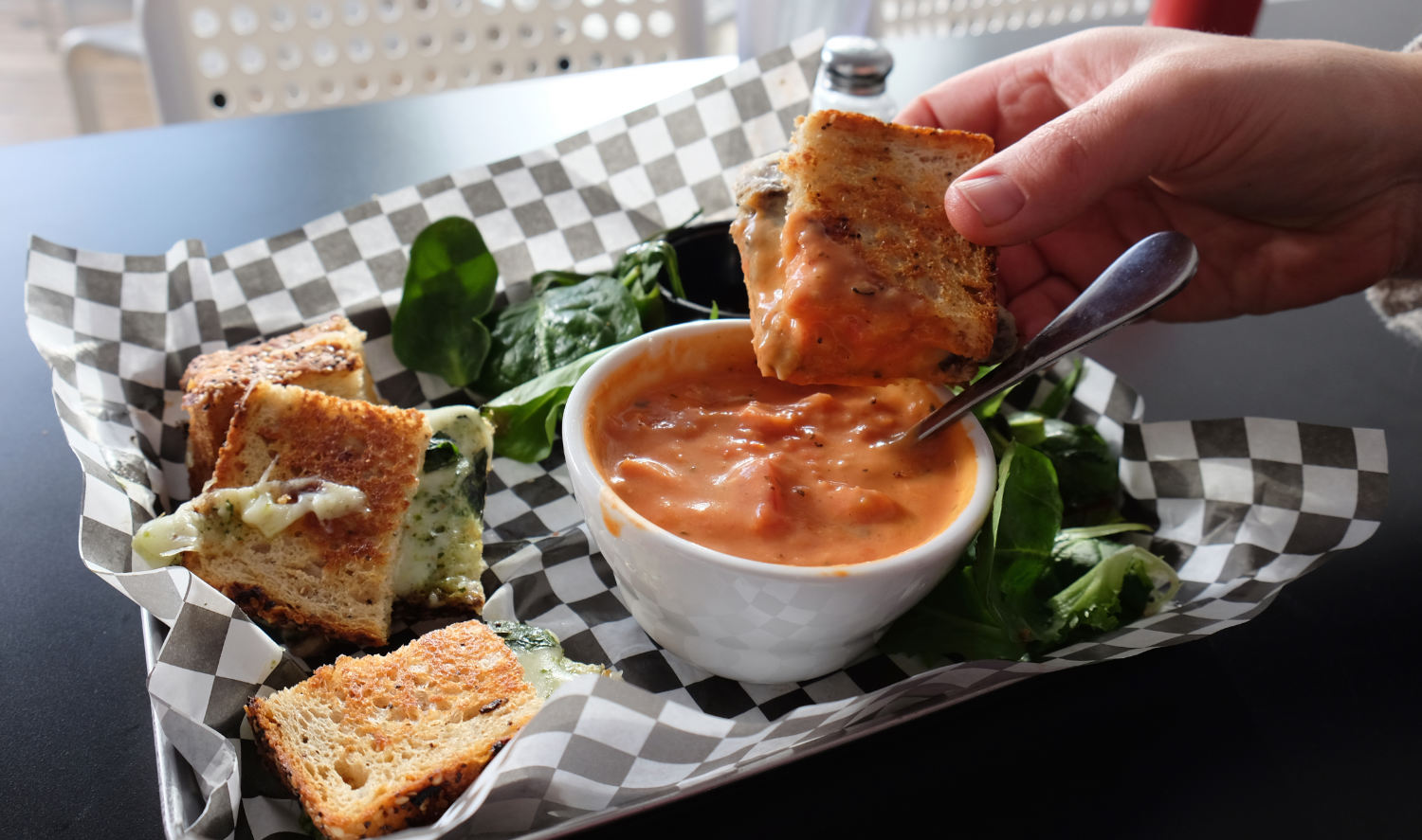 hand dipping grilled cheese sandwich into cup of tomato soap
