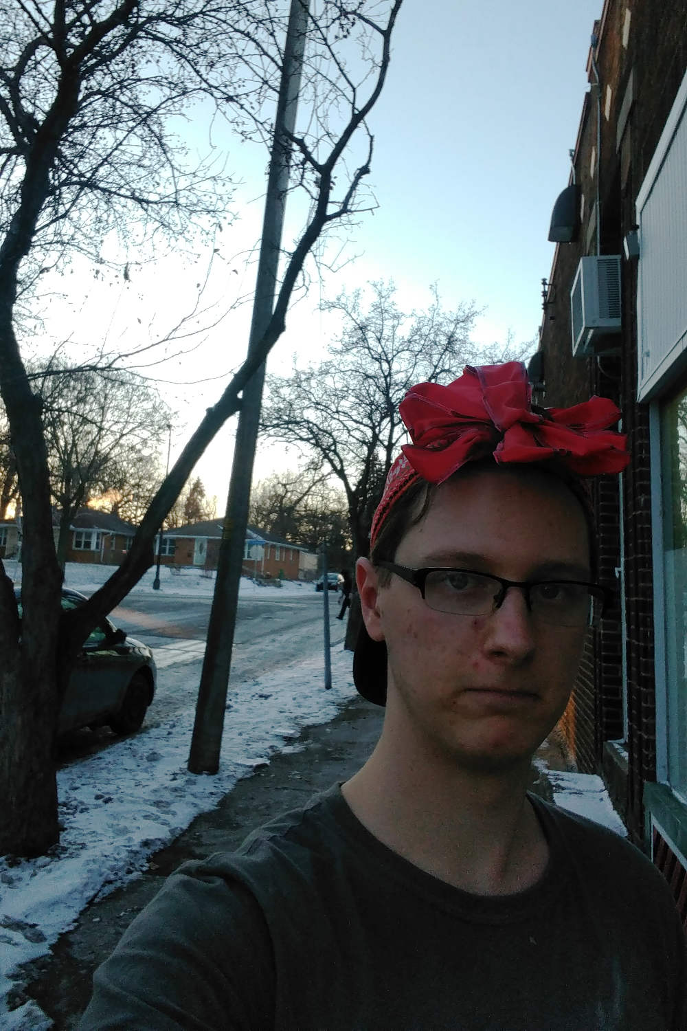 darkly lit man with red bow on head standing on a street of storefronts