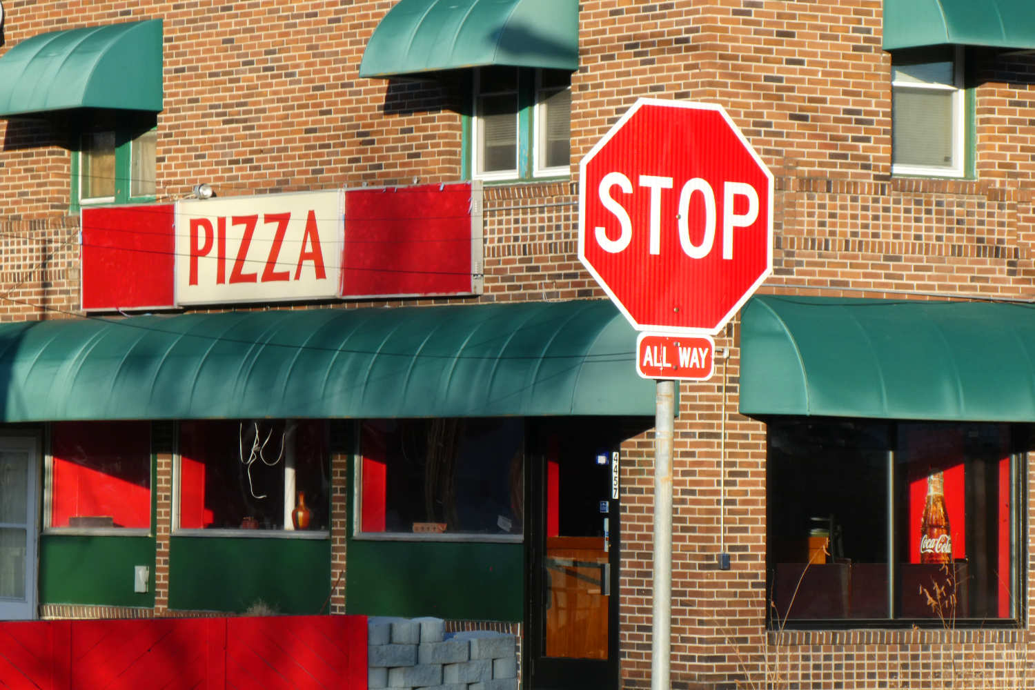 Red and white pizza sign on building with STOP sign in foreground