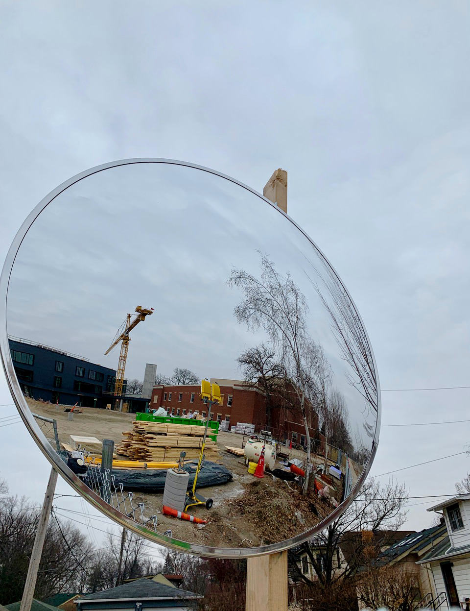 Convex mirror showing construction site with lumber, building materials, and a tall crane