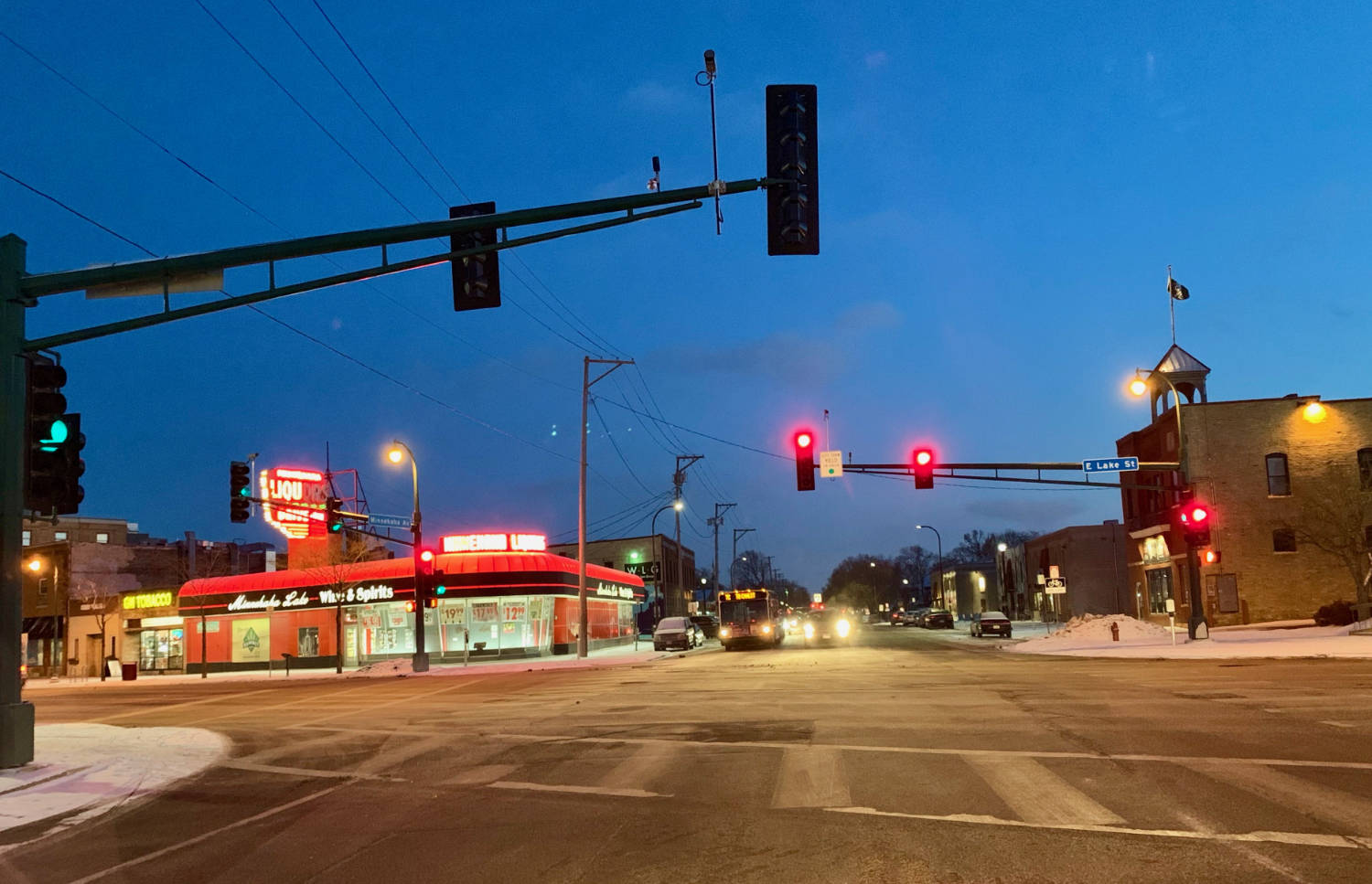 Traffic lights at intersection at dusk with Minnehaha Liquors lit sign on building in background