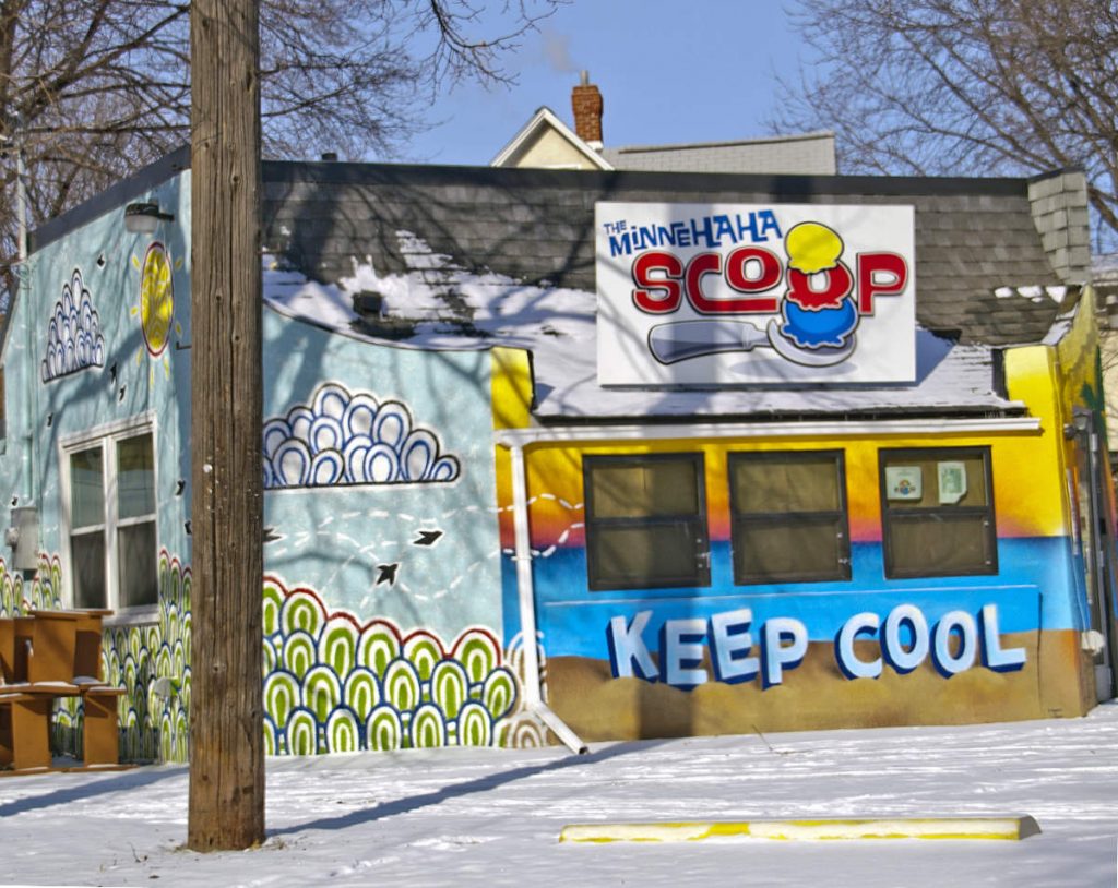Building with Minnehaha Scoop sign on top and Keep Cool mural on wall with snow in foreground
