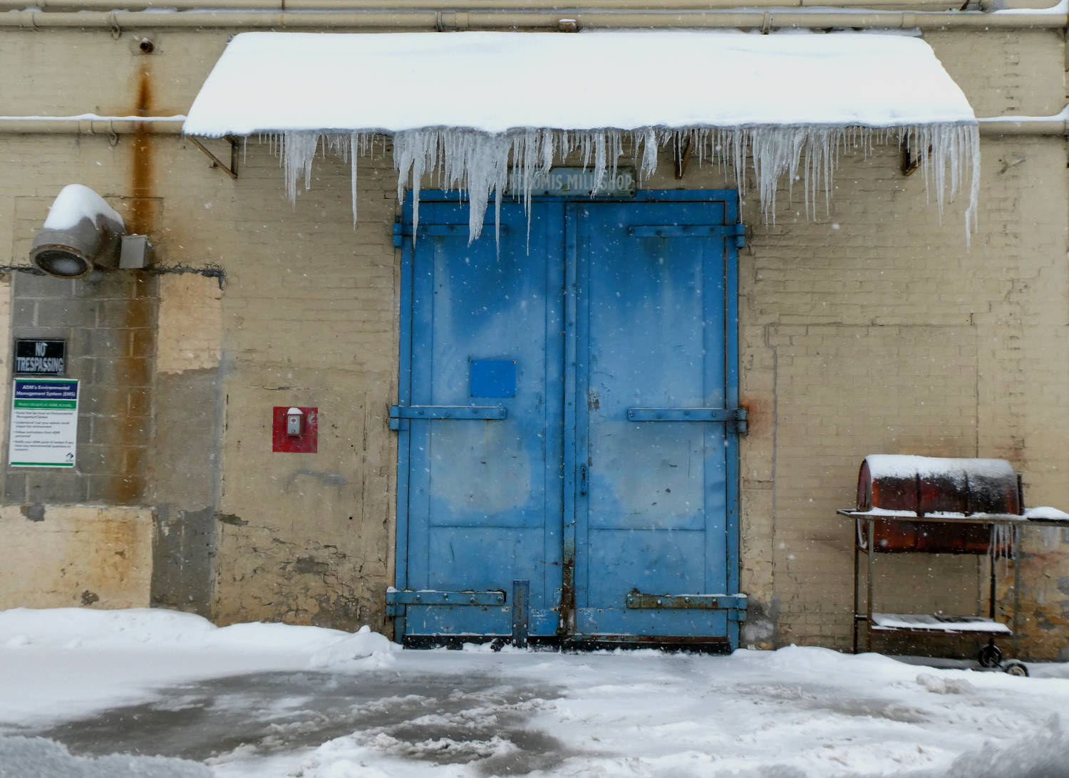 old, blue industrial double-doors with icicles on snowy overhang