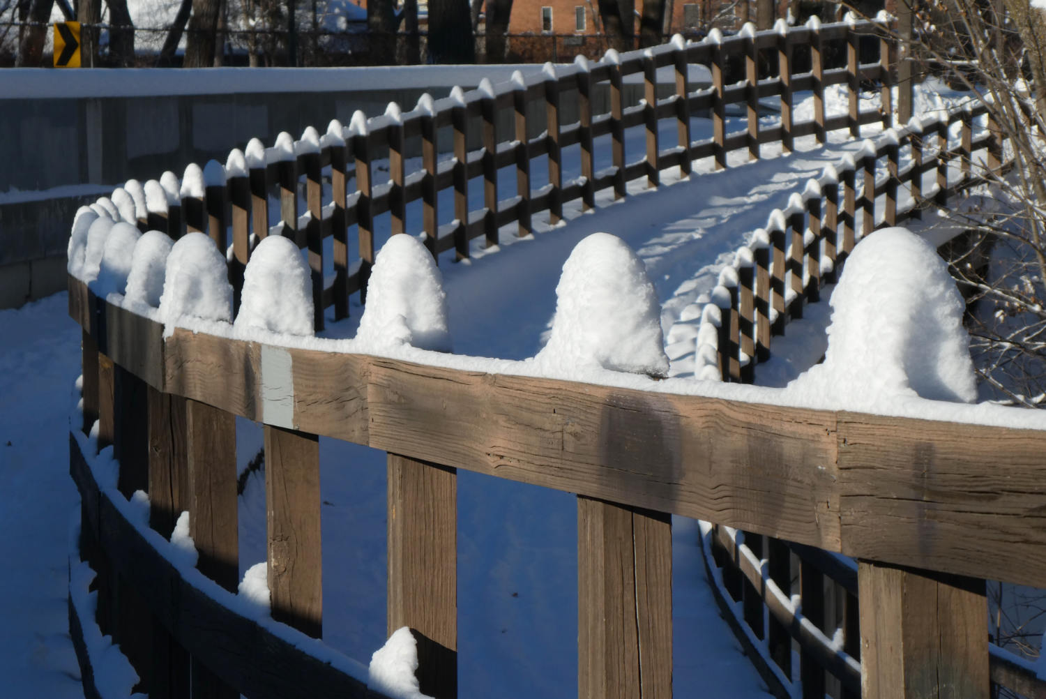 curving wooden railings with snow-capped posts on a sunny day