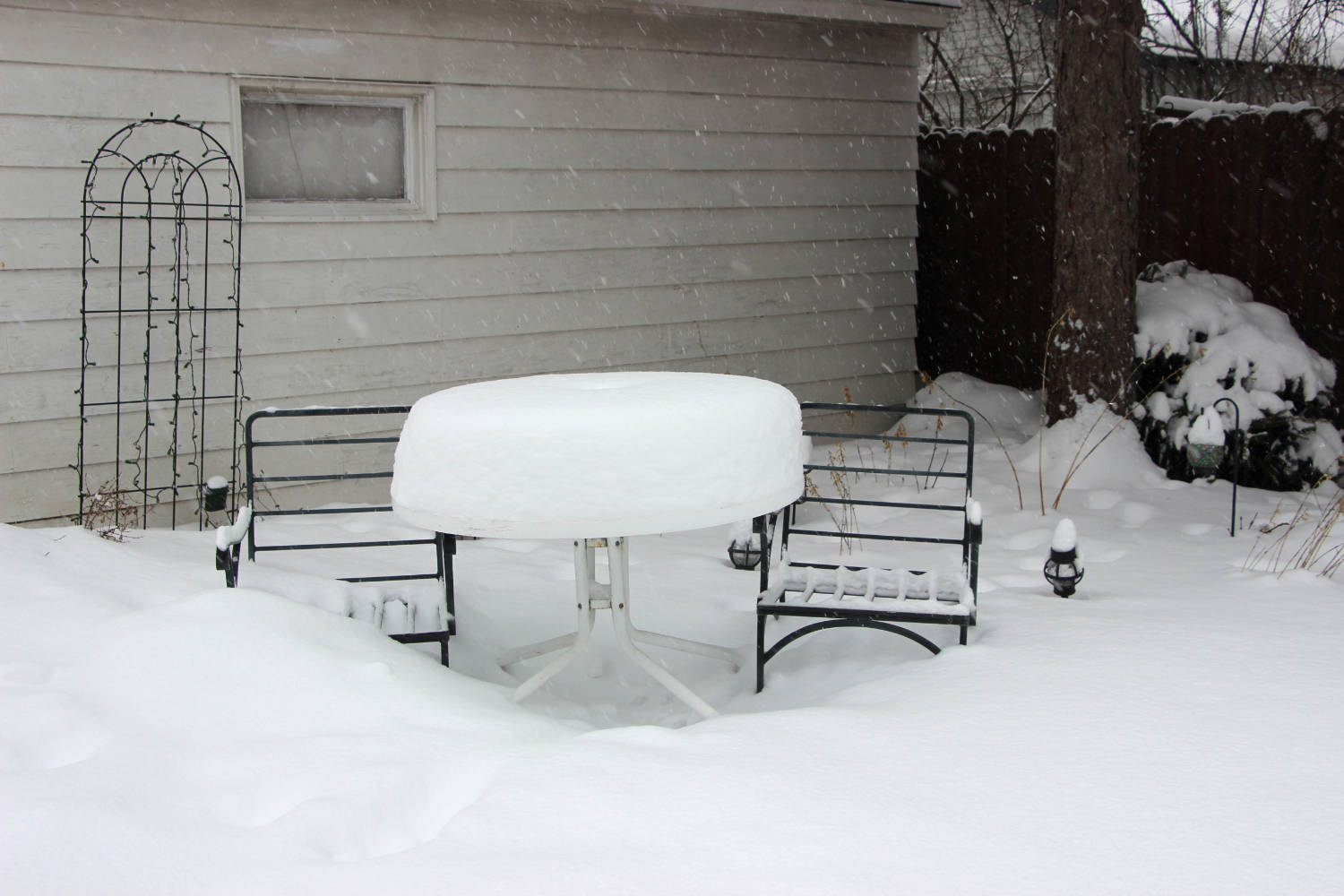 empty chair frames and table on patio covered with almost a foot of snow