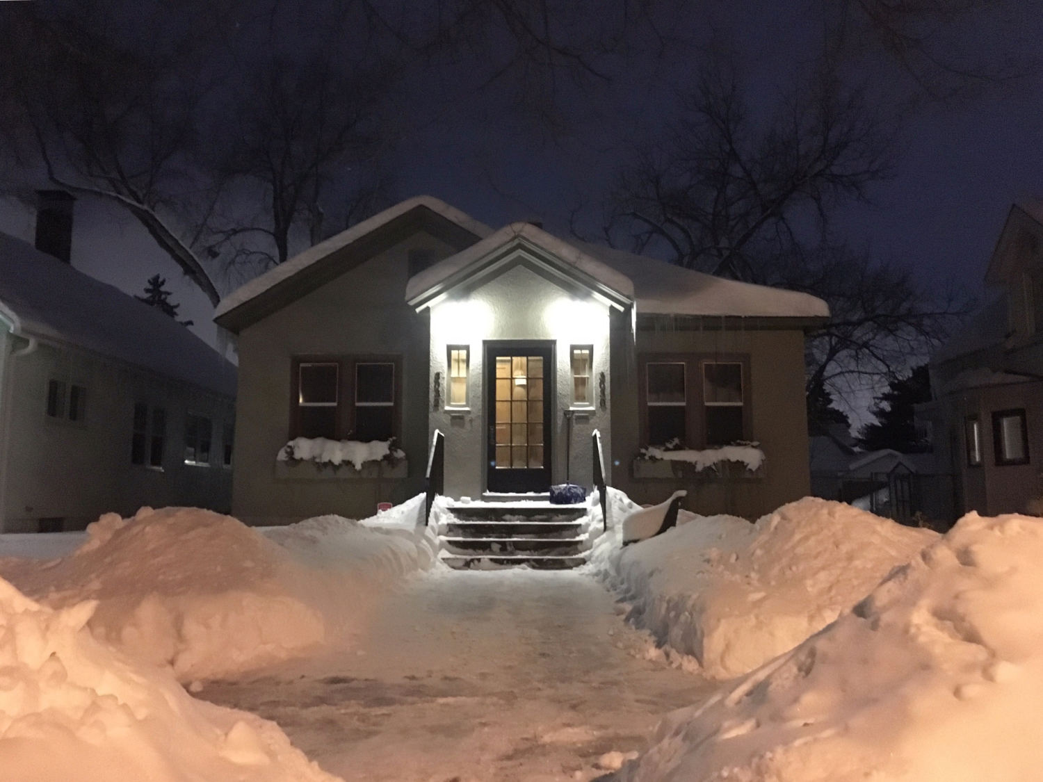 front of bungalow house at night with bright porch lights with snow