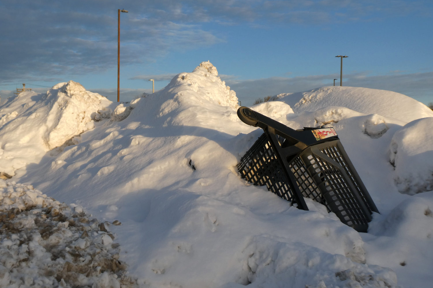 Tall mounds of snow with an inverted shop cart sticking out against a blue sky