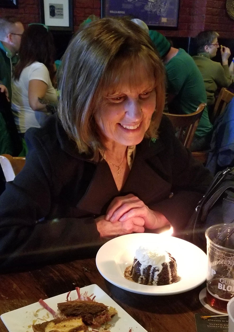 Smiling woman with face lit by a birthday dessert with candle in a restaurant