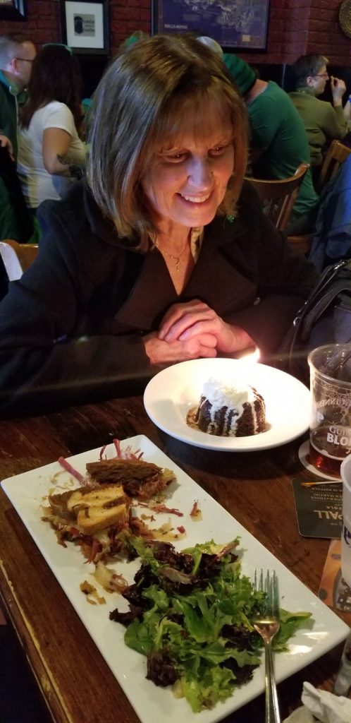 Smiling woman with face lit by a birthday dessert with candle in a restaurant