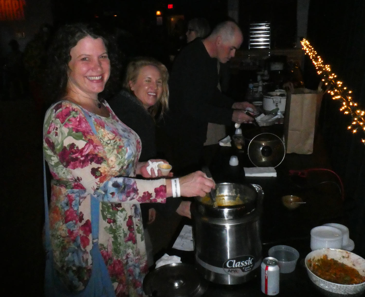 two smiling women at a buffet table serving themselves from a big pot