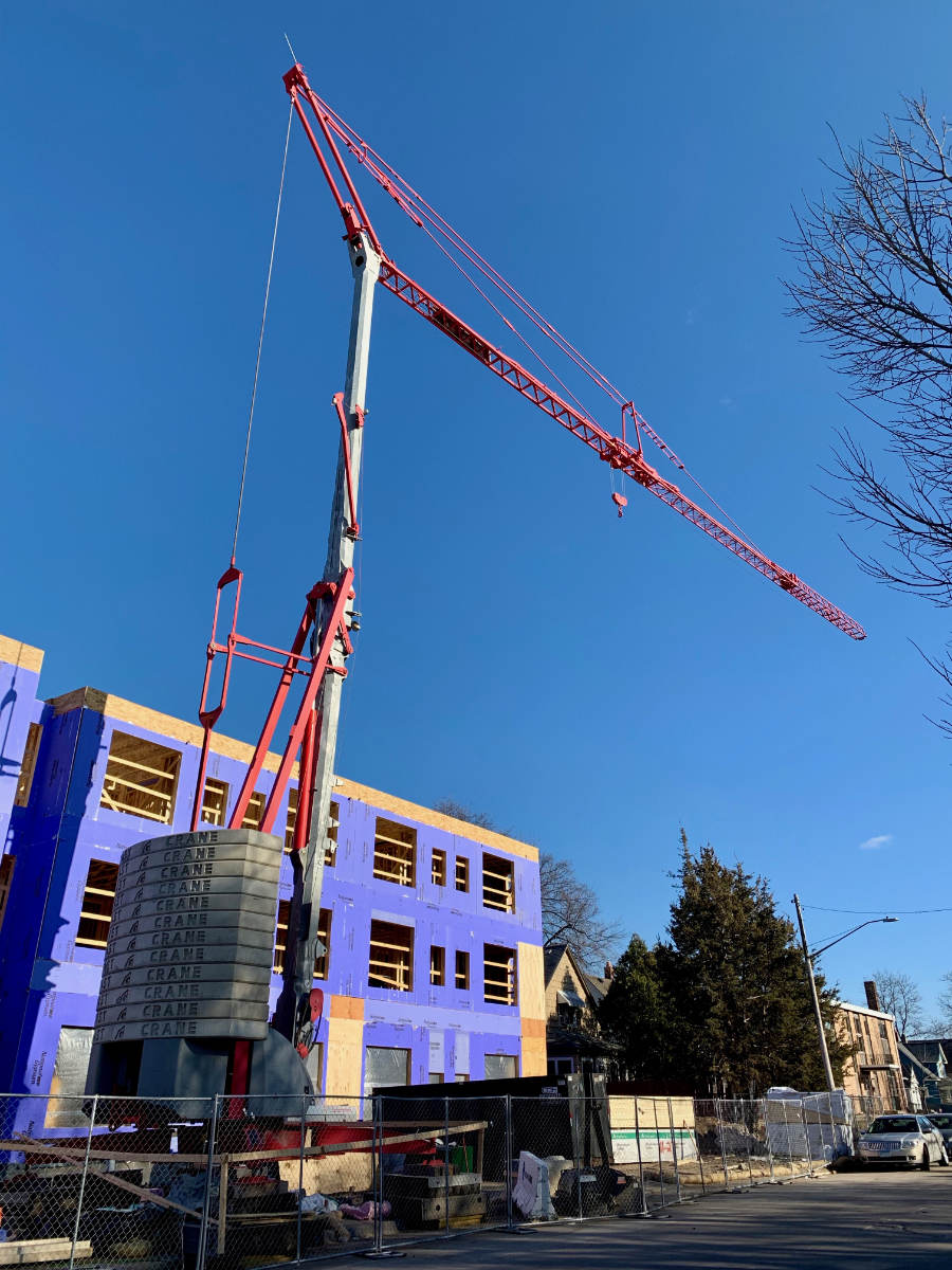 looking up at tall crane in front of a three-story building under construction with purple insulation on exterior walls