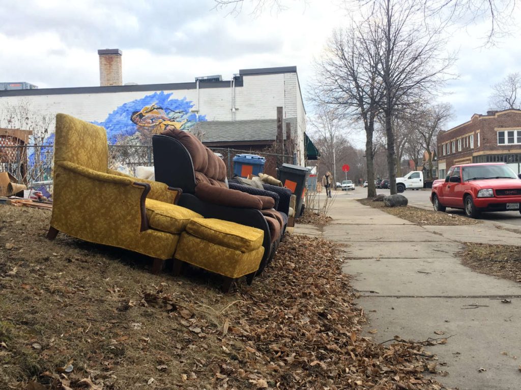 old stuffed couch and sofa next to sidewalk with mural on building in background