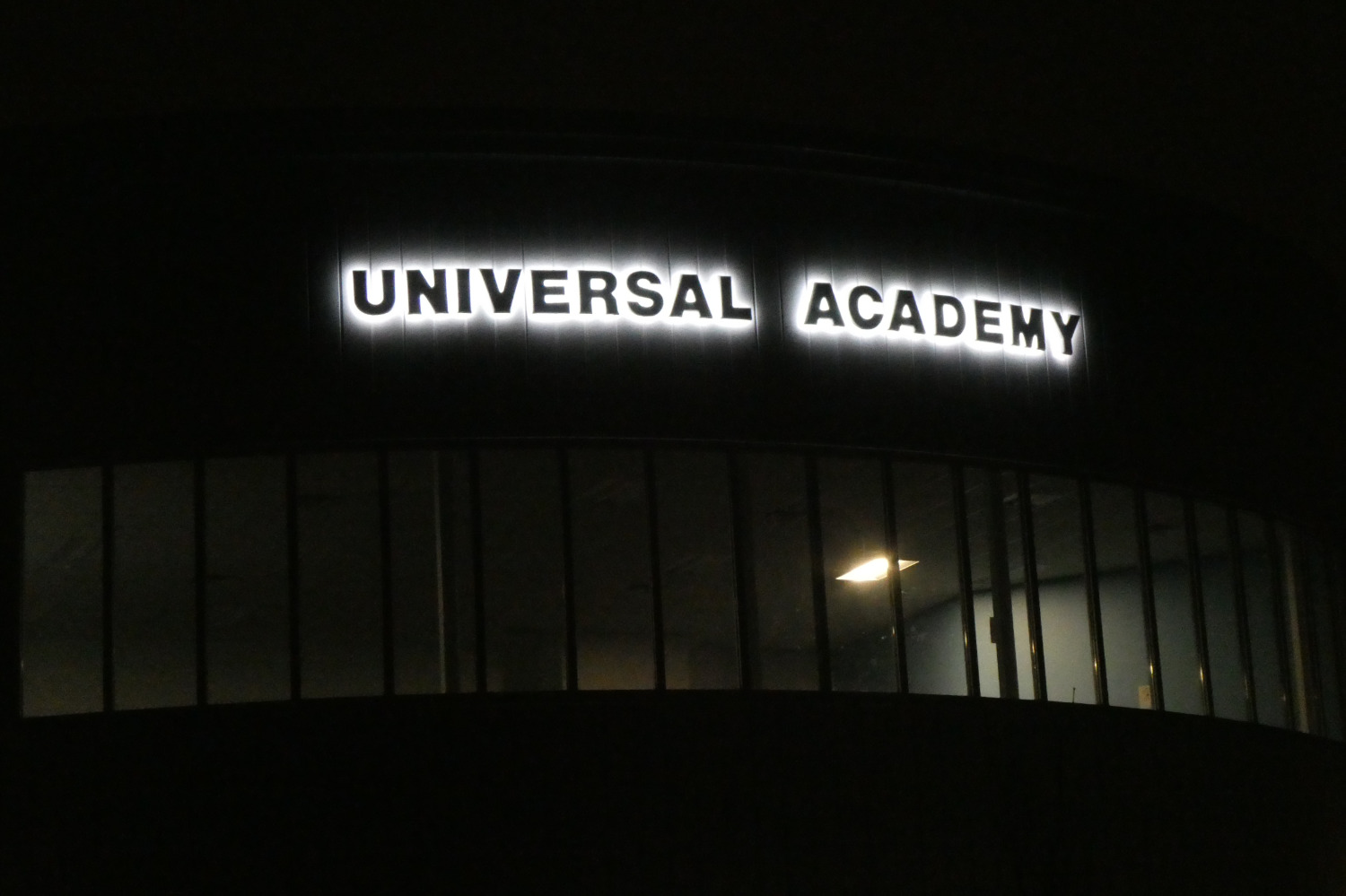 The words "UNIVERSAL ACADEMY" backlit at night in the dark.