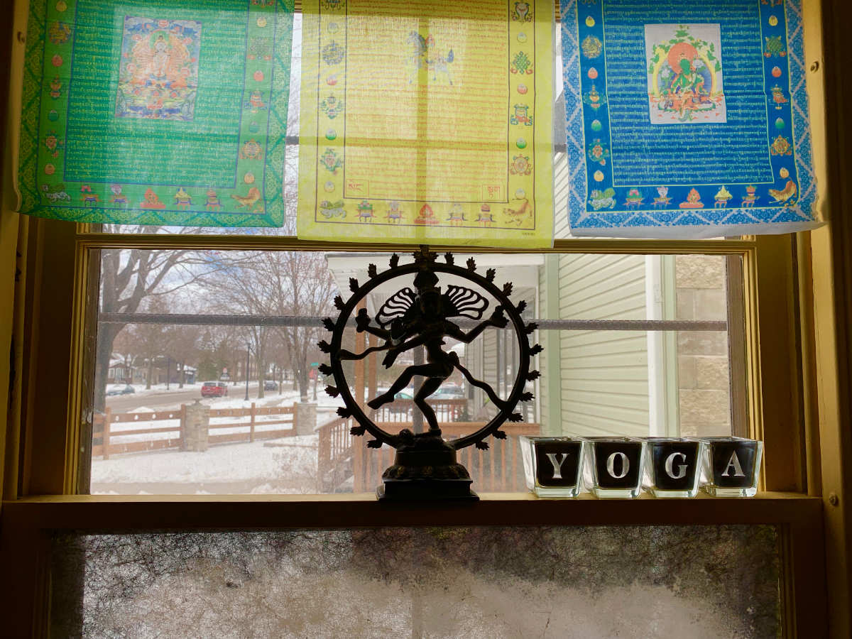 looking out a window with translucent green, yellow, and blue tapestries in upper pane and a statue silhouette of a figure with outstretched limbs in a wheel shape