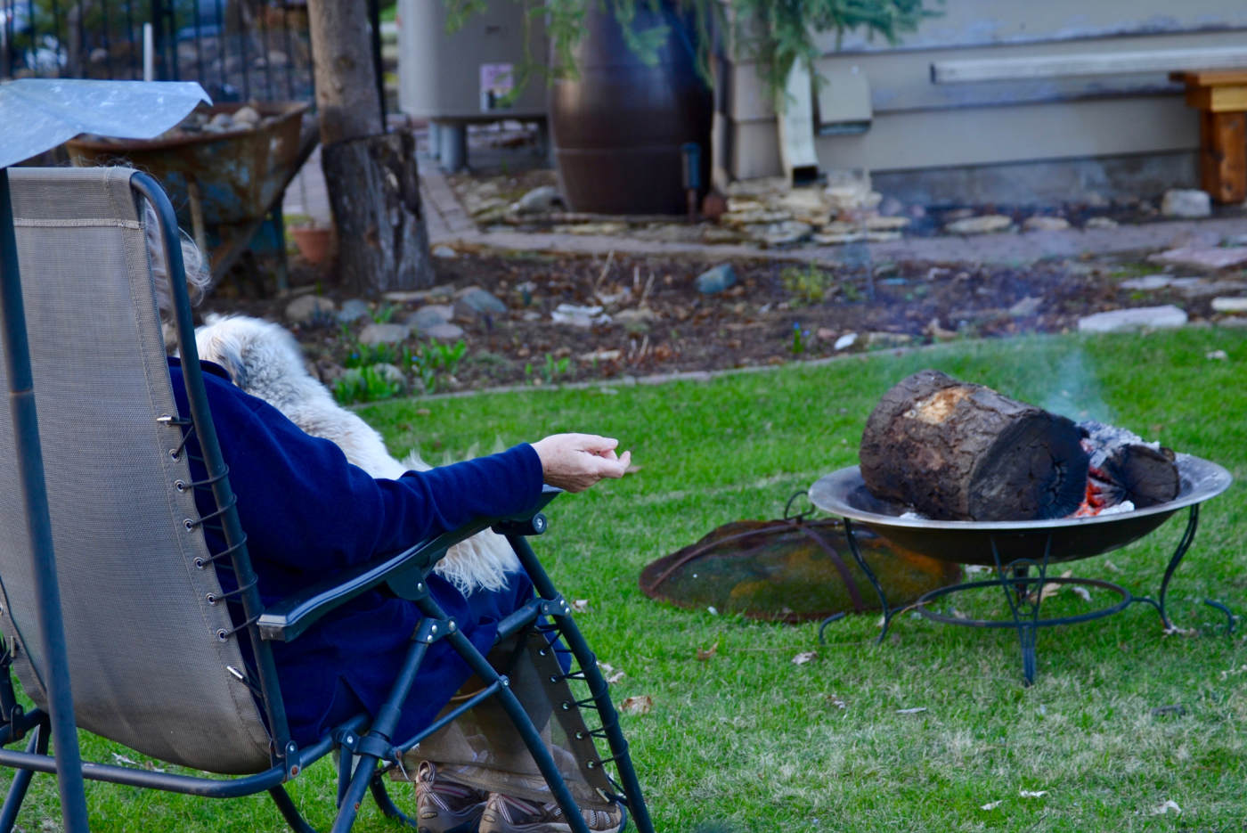 backside of person sitting in a lawn chair next to a fire pit with smoldering log sections