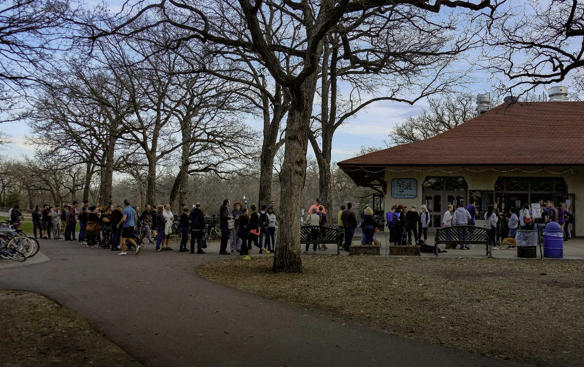 Long line of people standing outside a park building with bare trees around them