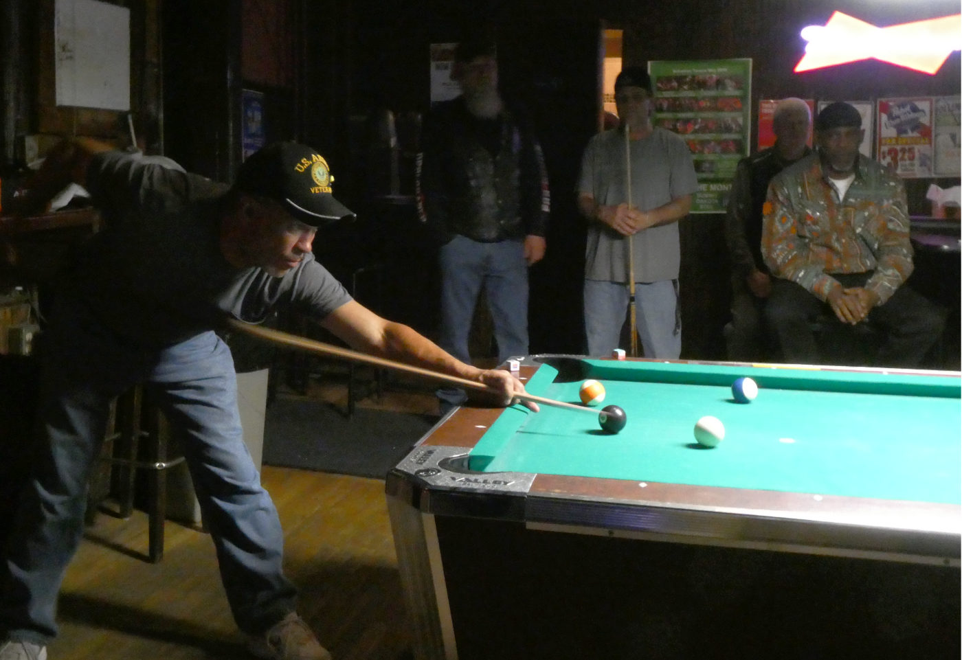 Man leaning over readying a shot on a pool table as three others look on