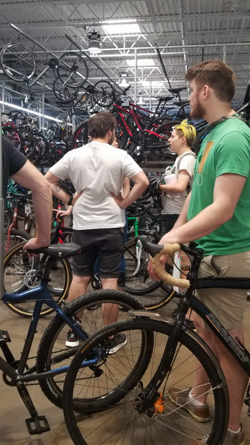 several people standing with bicycles with racks of many bicycles behind and overhead