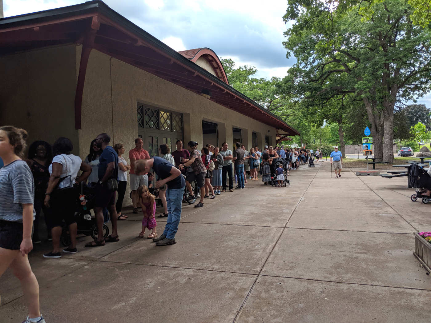 long line of people outside a park building on a summer day