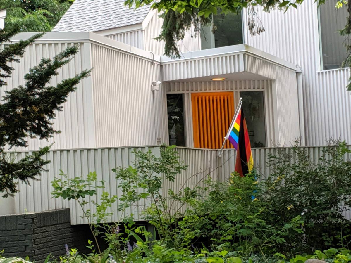 Back porch of a white house with a rainbow Pride flag hanging over the railing