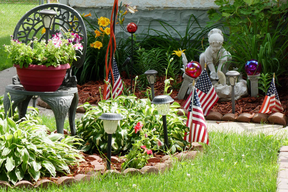 hosts and potted flowers with four small USA flags, glass globes and a cement statue of little girl in garden