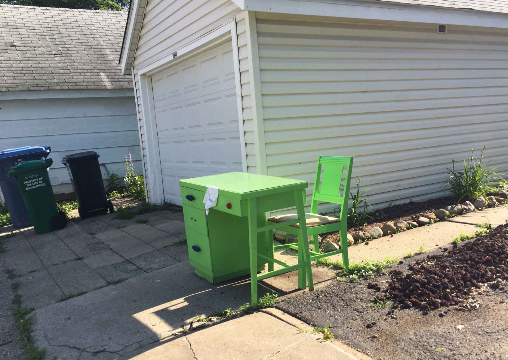 bright light green desk and chair in sun next to a white garage in shade