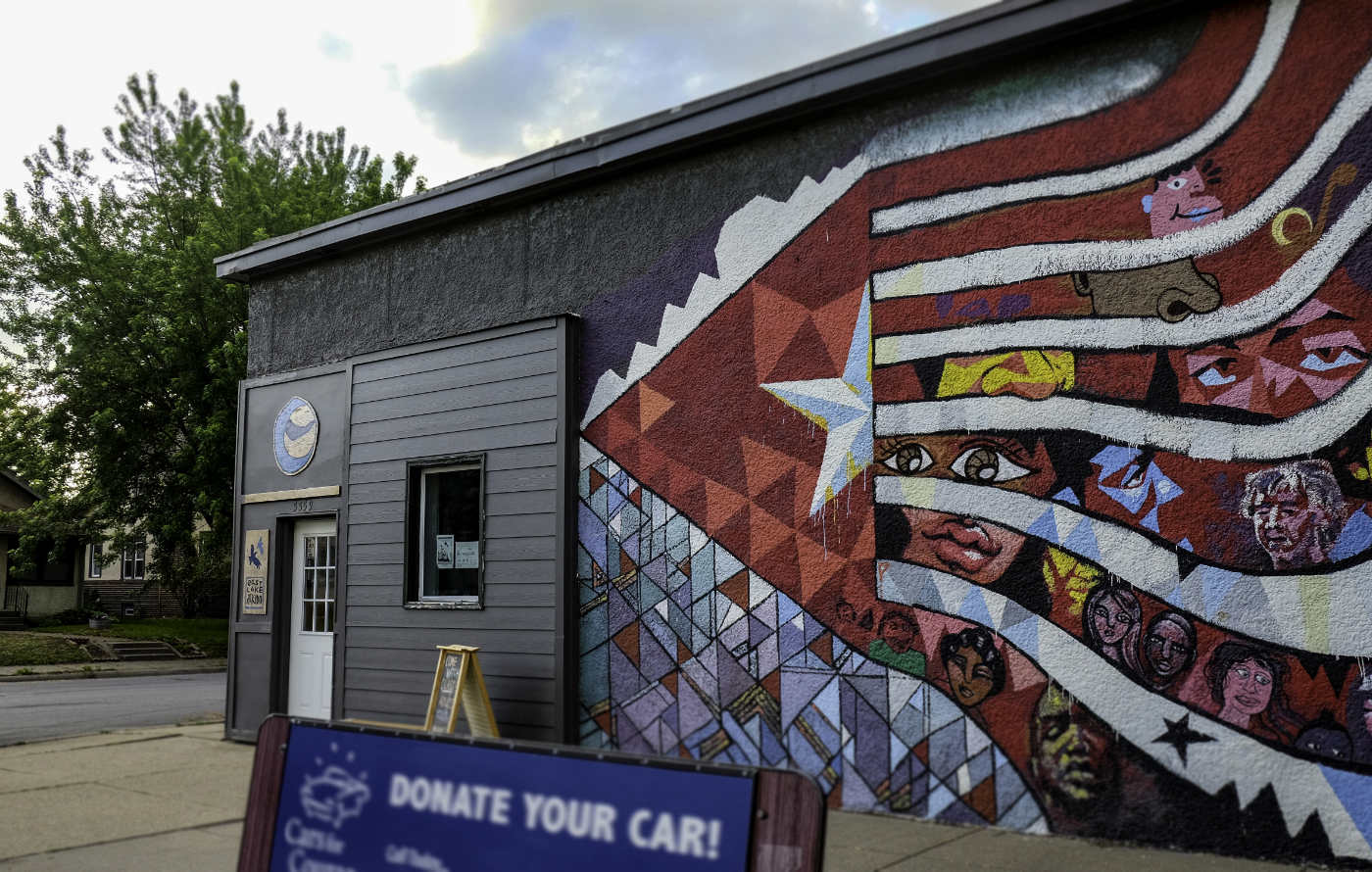 Gray building with mural depicting a diversity of faces in an abstracted flag design with red , white, and blue colors
