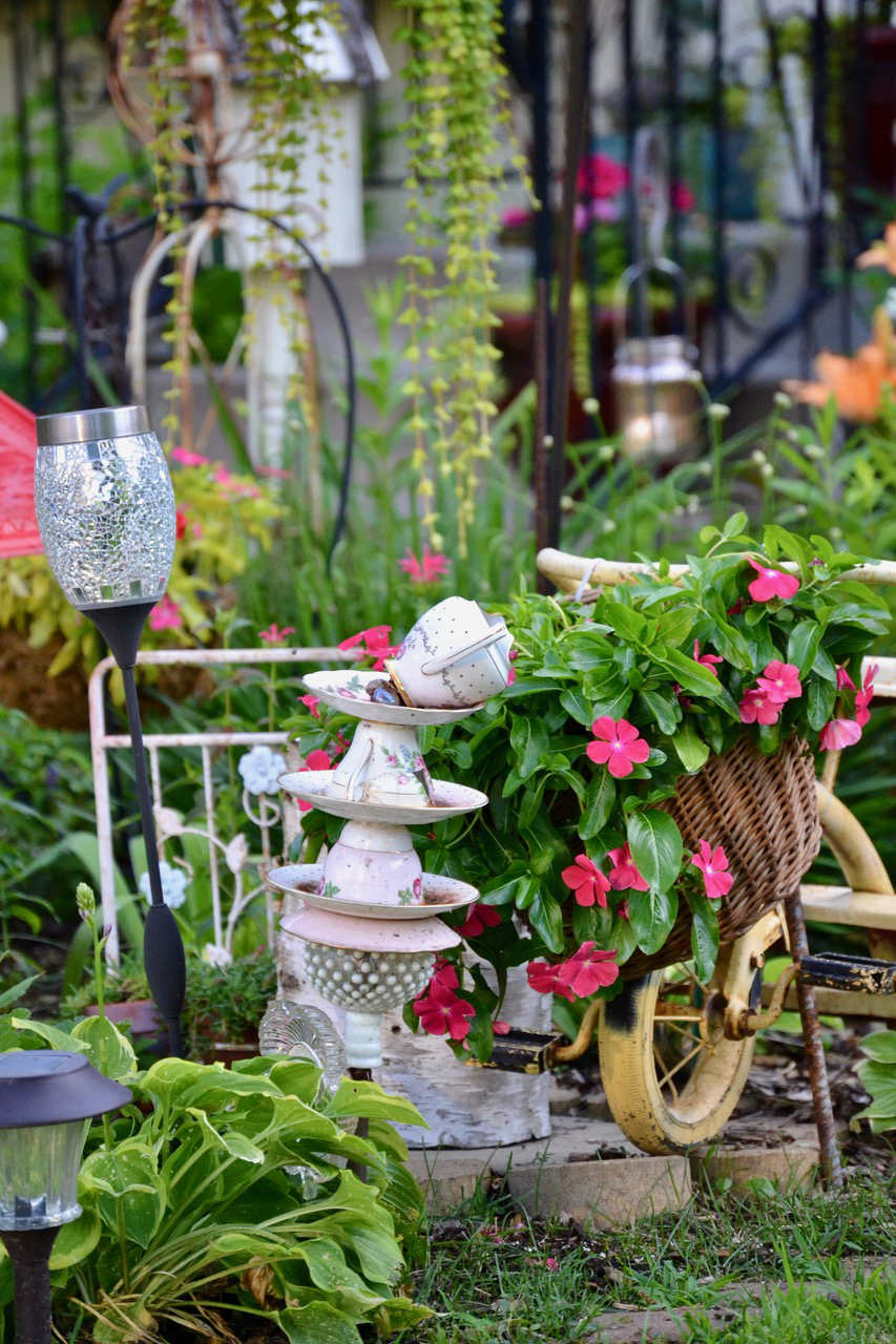 Crafted stack of floral china teacups and creamer in a garden setting with a basket of pink impatiens
