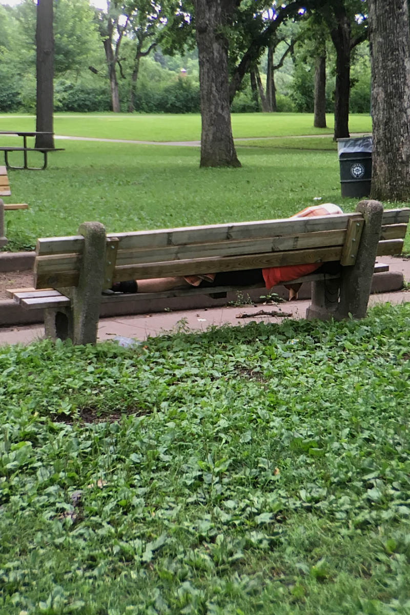 park bench from behind in a green field with a person laying flat on the bench