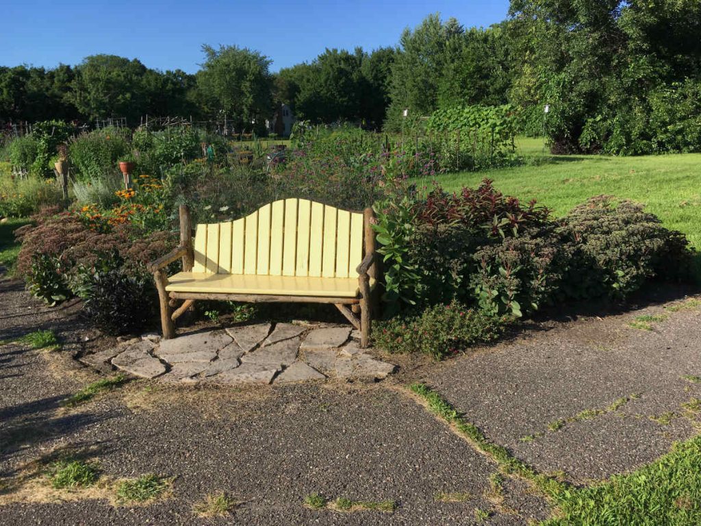 pale yellow bench on stonework with bushes, green field and trees