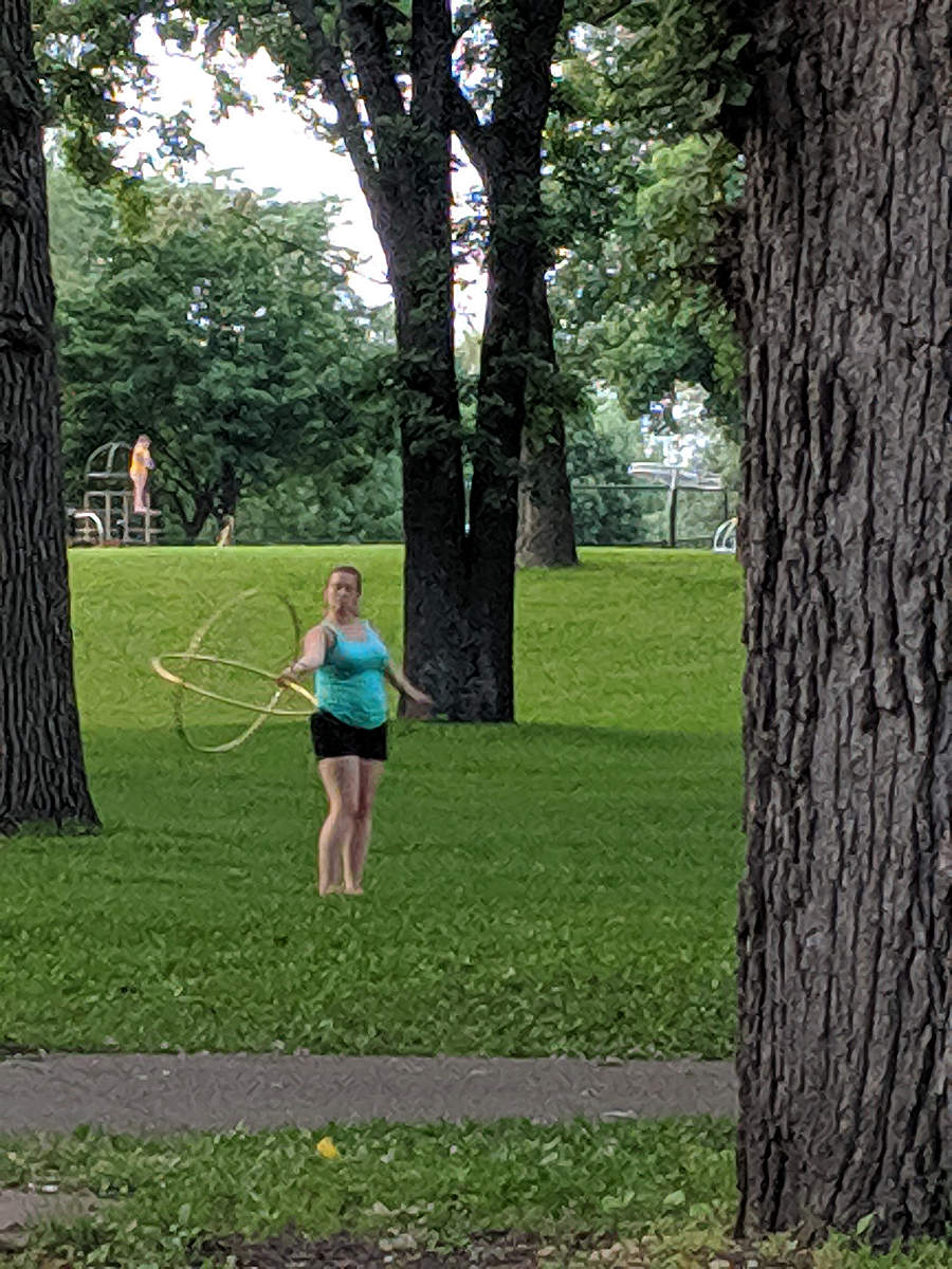woman with two hula hoops on grass with some tree trunks