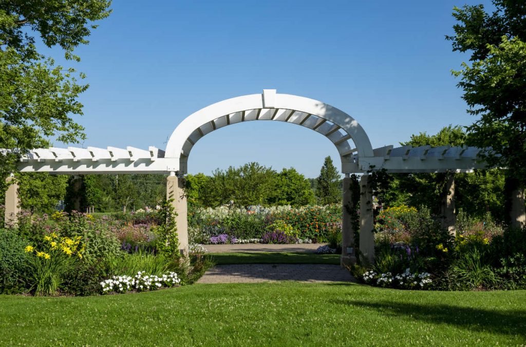 white archway with pergolas as entrance to a large flower garden 