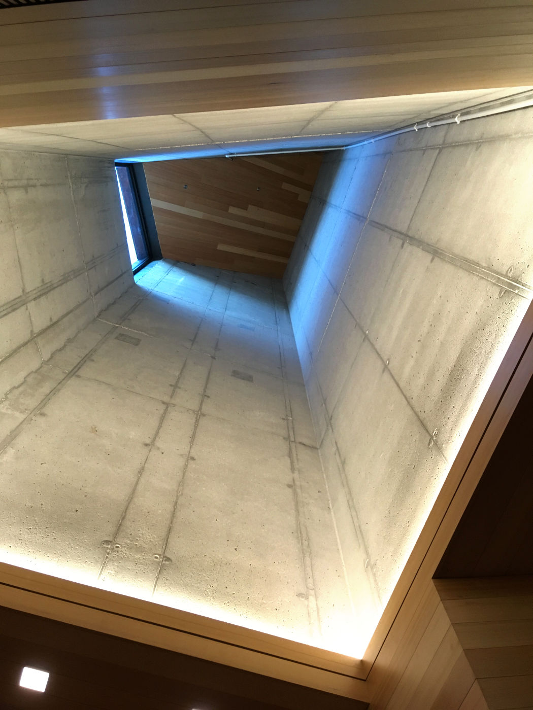 looking up a trapezoidal cement spire with blue light at the top illuminating a wood paneled ceiling