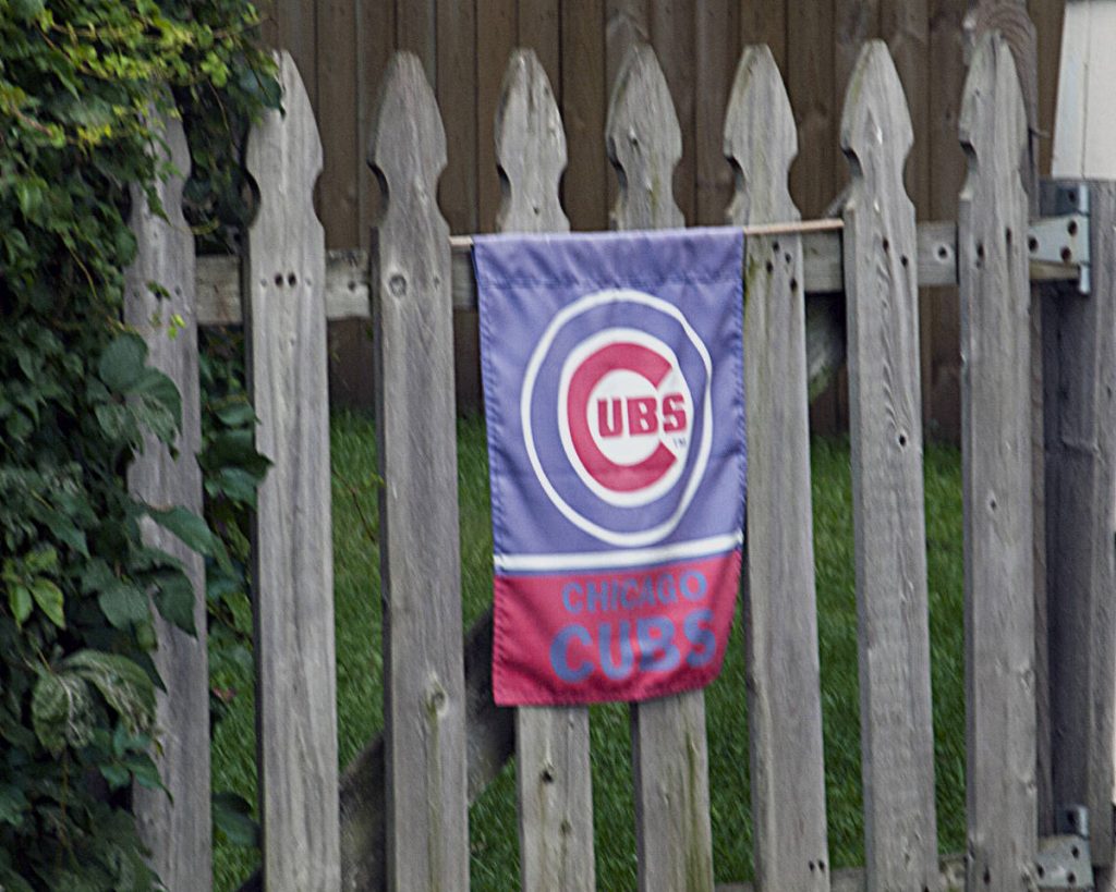 Red, white and blue Chicago Cubs pennant flag hanging on a bare wood picket fence 