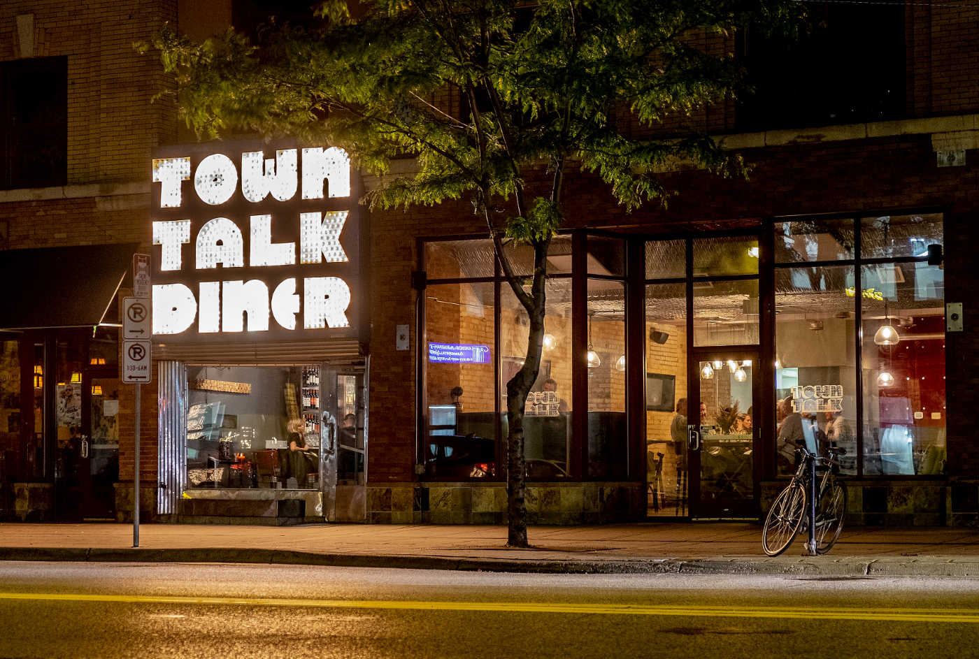 nighttime street scene of a lit-up storefront with a large bright sign reading TOWN TALK DINER