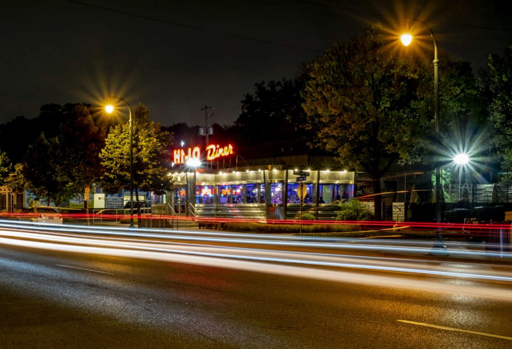 Neon-lit diner at night with blurred car lights in foreground
