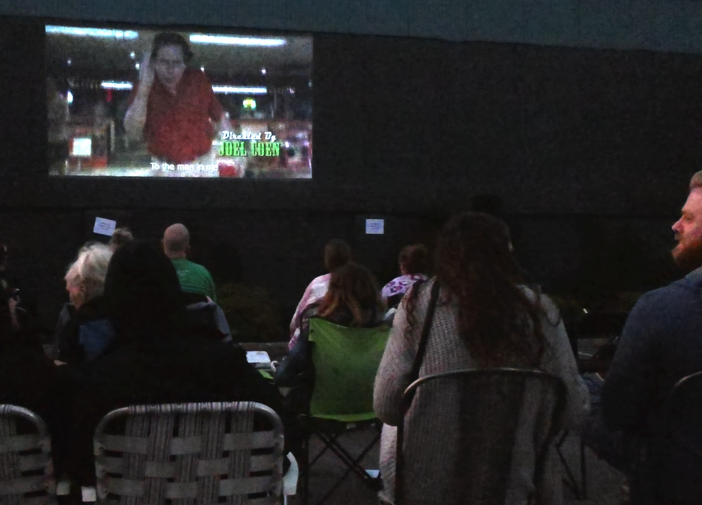 backs of heads with a small group at night watching a movie on a screen