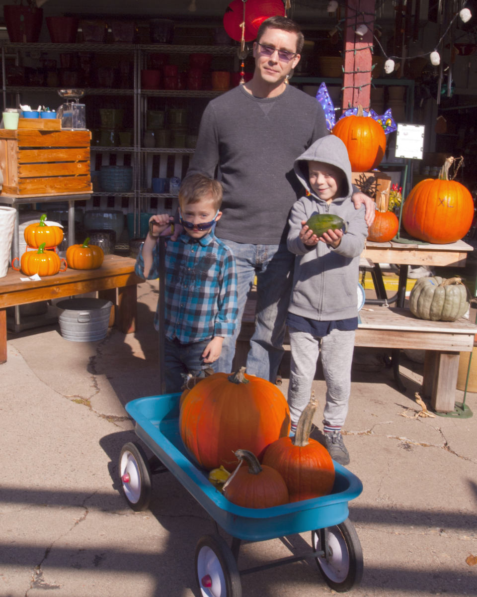 Two boys with a wagon of pumpkins with a man and lots of orange pumpkins around them