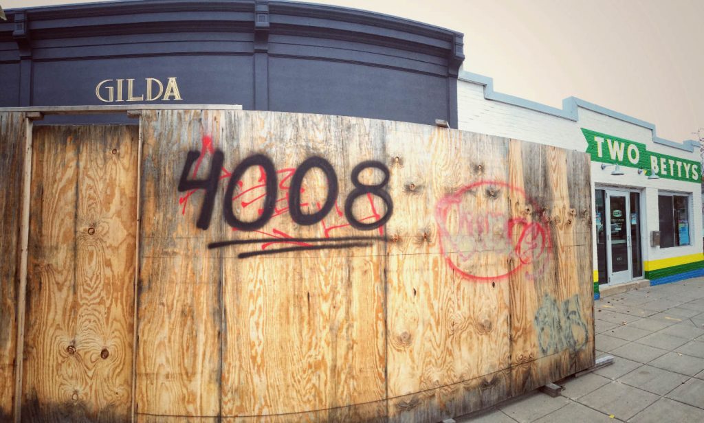Wooden wall outside a storefront with 4008 spray-painted in black with gold GILDA sign above