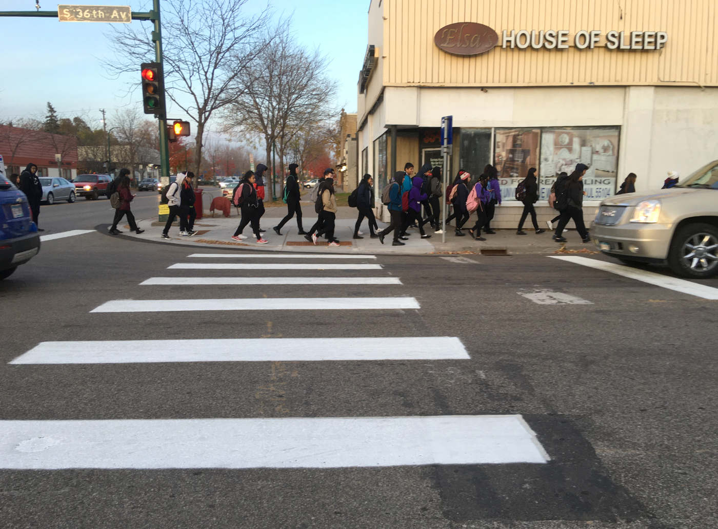 Line of young people walking on a sidewalk across a street with a House of Sleep building on the corner and painted crosswalk in the foreground