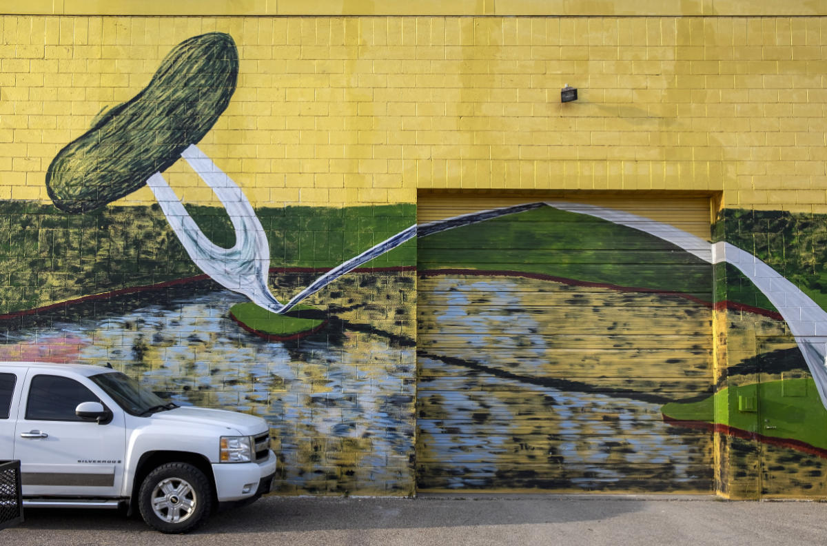 Brick wall with painting of arched fork with a pickle on the end, and a truck parked in foreground